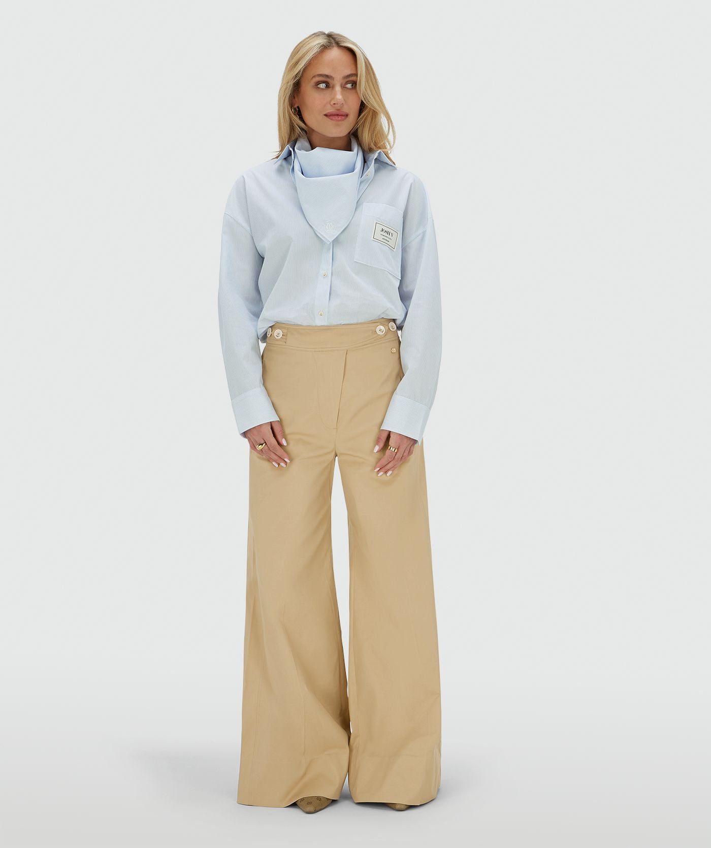 Image 28: Het model draagt een oversized blauwe blouse met borstzak, inclusief het bijpassende sjaaltje