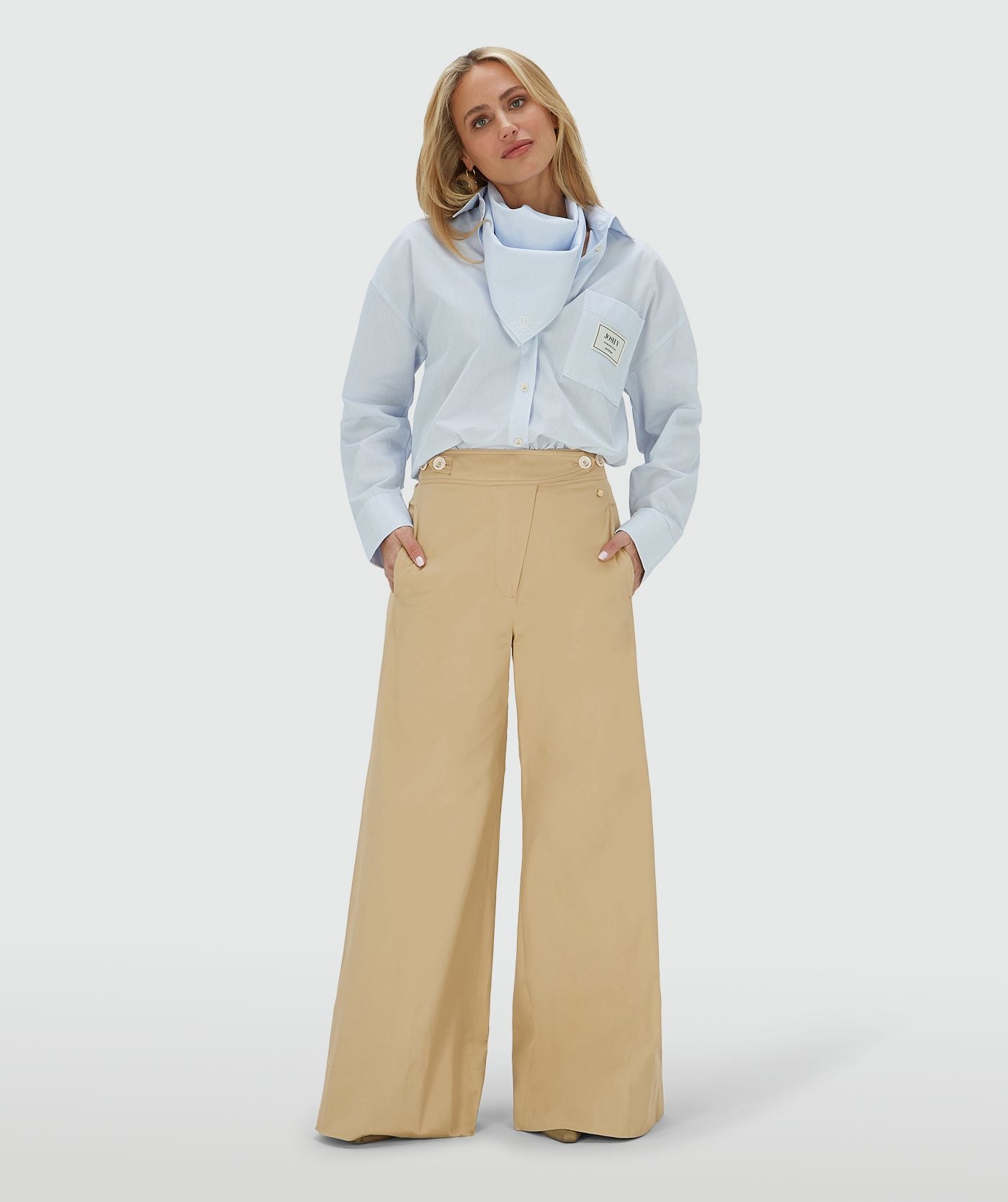 Image 1: Het model draagt een mid rise wide leg pantalon in de kleur Light Camel, voorzien van verstelbare knopen in de tailleband