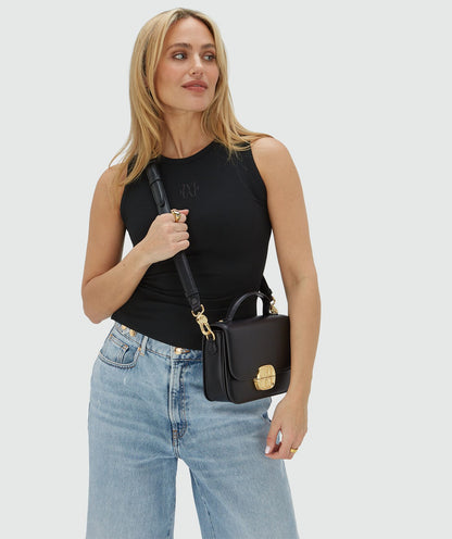 Image 11: Het model draagt een tas in het zwart met een goudkleurige bucklesluiting crossbody