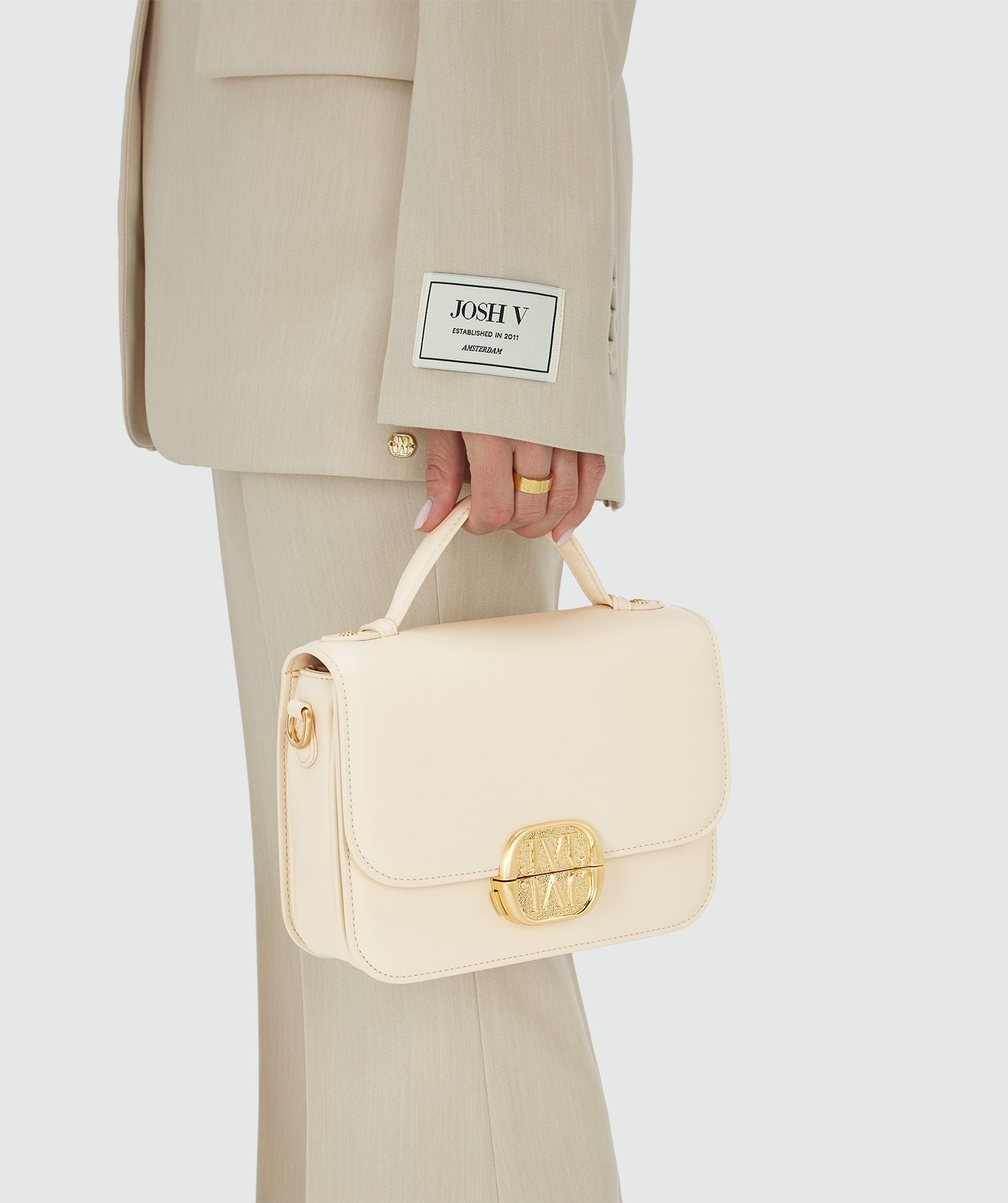 Image 11: Het model houdt een tas in Crème White met een goudkleurige bucklesluiting vast aan het handhengsel