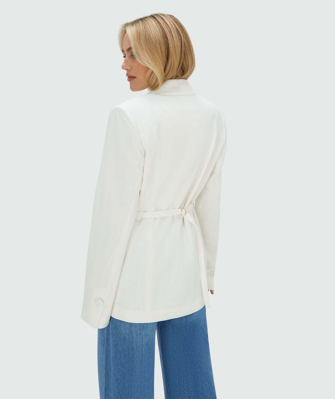 Image 7: Achteraanzicht van het model in een Off White oversized blazer, waarbij de ceintuur aan de achterzijde zorgt voor een getailleerd effect