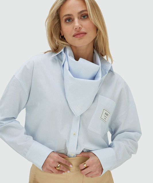 Image 22: Het model draagt een oversized blauwe blouse met borstzak, inclusief het bijpassende sjaaltje