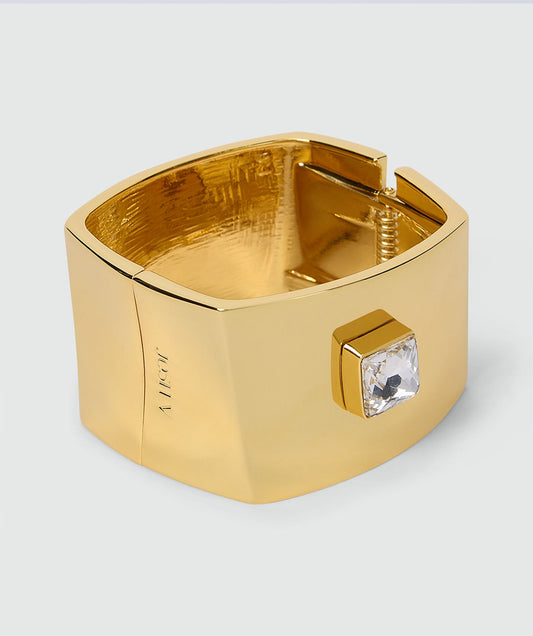 Image 3: Goudkleurige armband met brede band, vierkante transparante steen en veersluiting, afgewerkt met een subtiel JOSH V-logo aan de zijkant zonder model, weergegeven op een lichtgrijze achtergrond